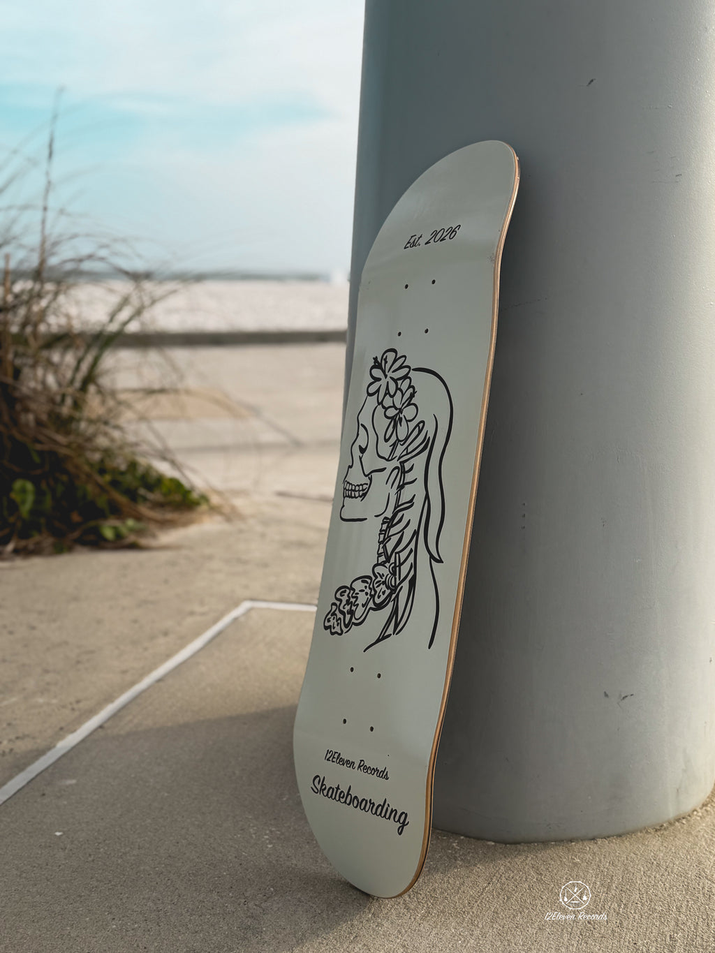 Skateboard deck with a design leaning against a pole on a beach.